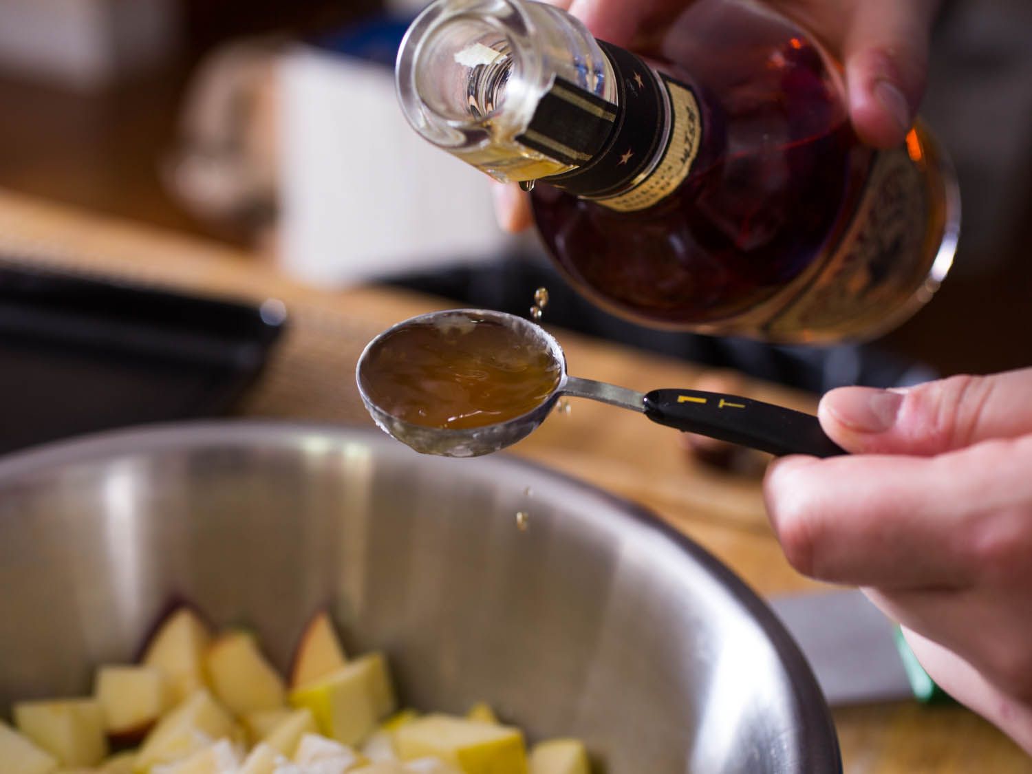 Pouring whiskey into a tablespoon measure to add to apple crisp filling.