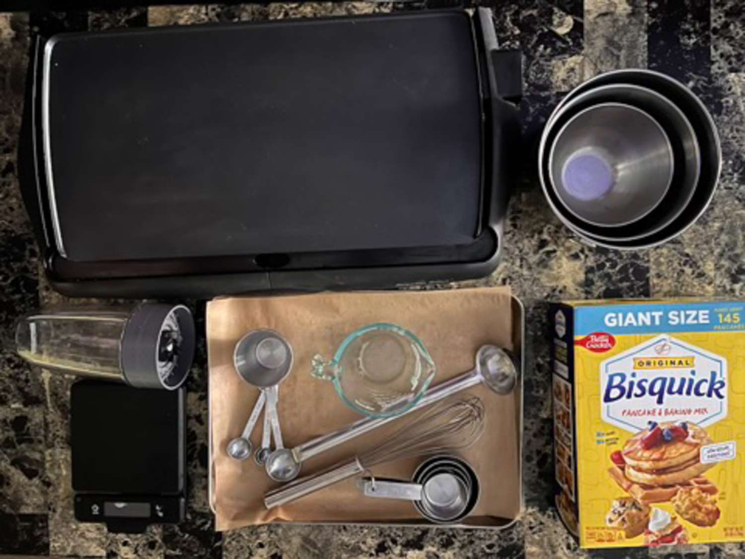 A sheet tray with measuring cups and spoons and a box of pancake mix