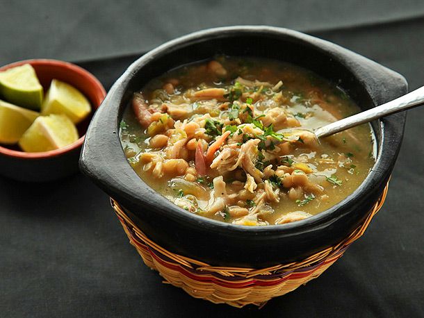A bowl of turkey white chili with lime wedges on the side garnished with herbs