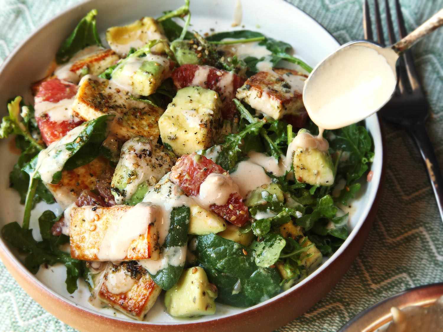 The composed salad being drizzled with the dressing with a metal spoon.