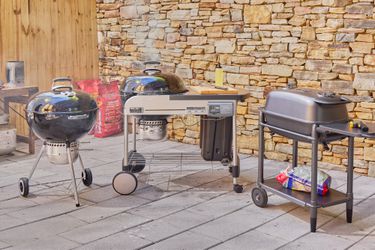Three charcoal grills on an outdoor patio.