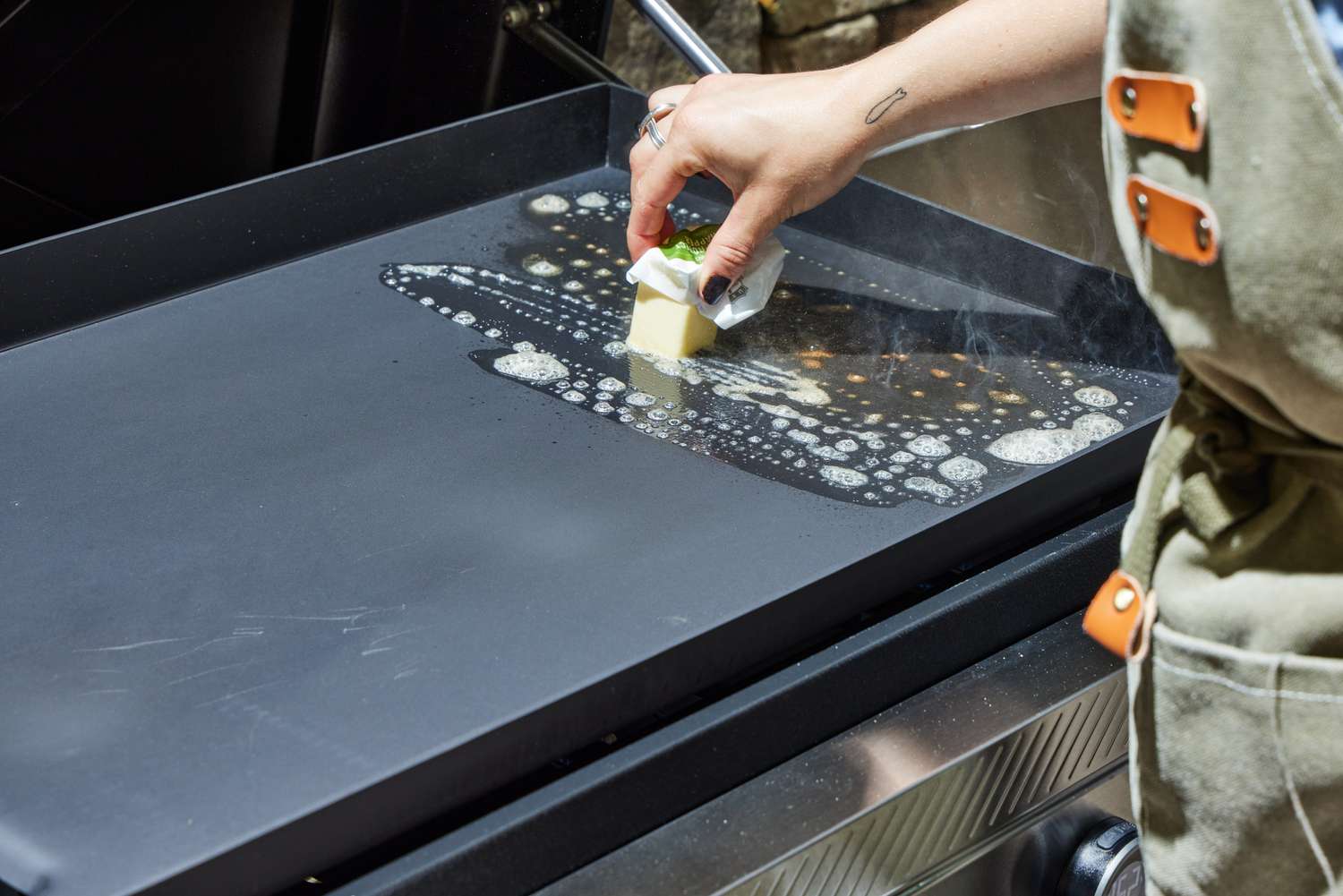A person melts butter on the top of the Weber Slate 30 Inch Griddle
