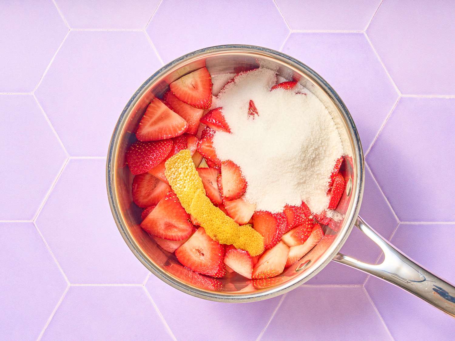 Cooking strawberries with sugar and a lemon peel in a saucepan