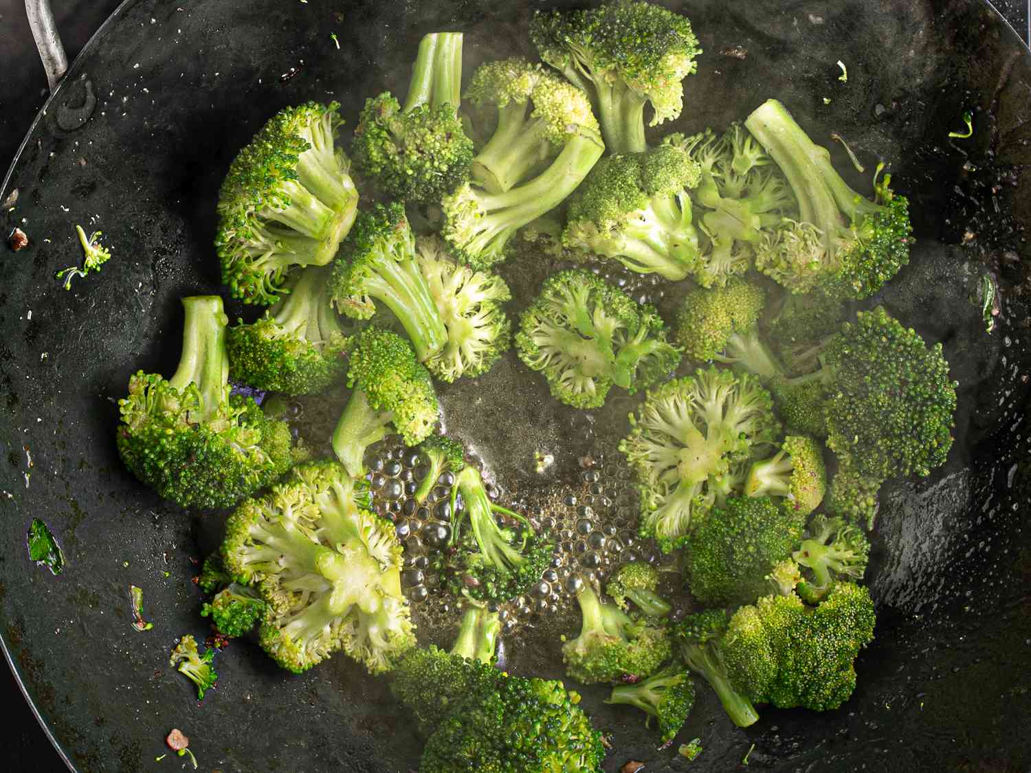 Â¼ cup of water added to broccoli inside wok, with the water boiling.