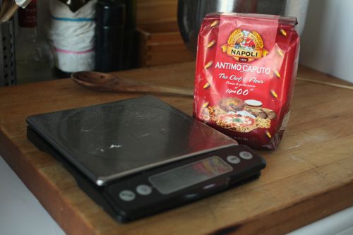 A bag of flour and a kitchen scale on the table. 