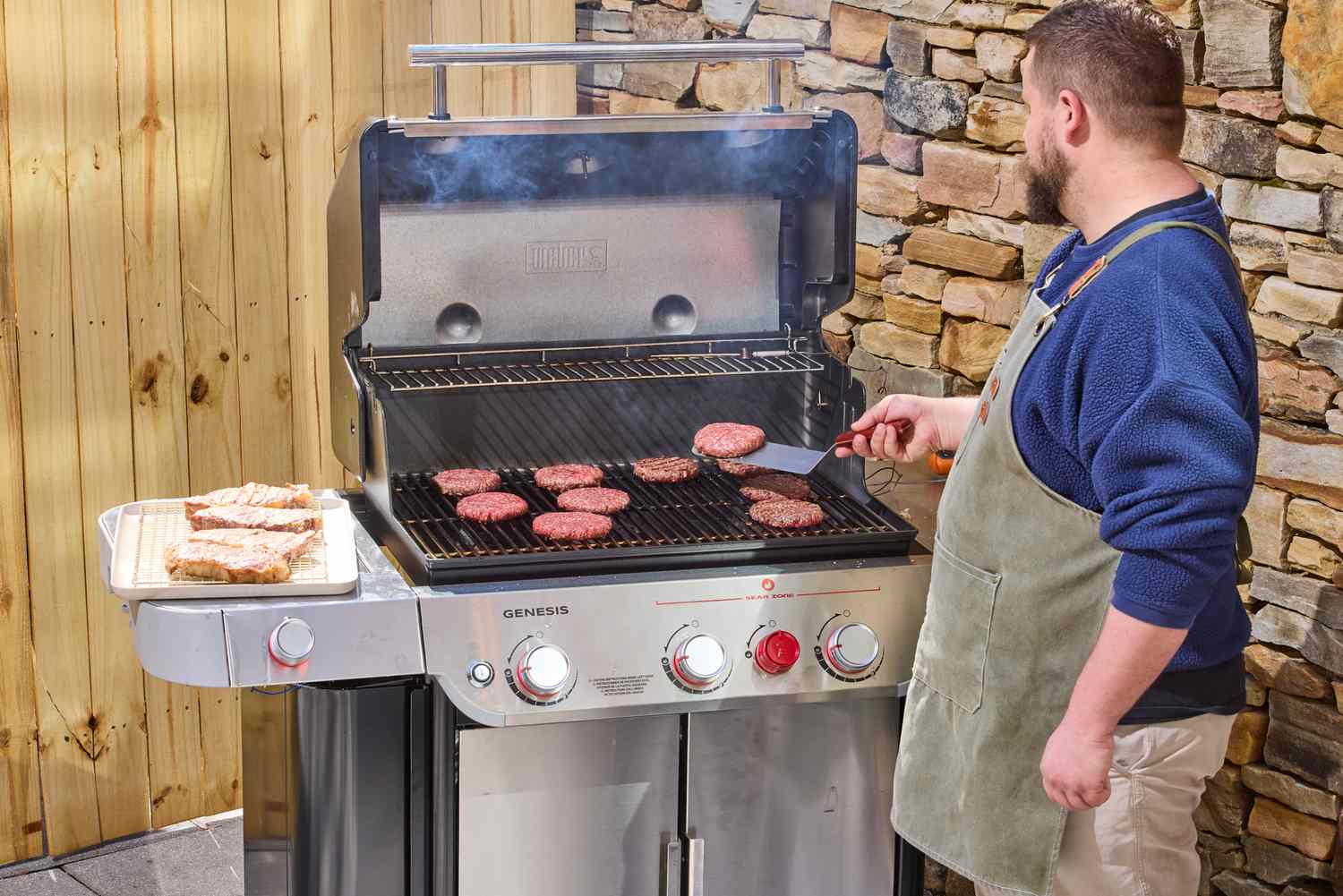 A person flipping the patties on the Weber Genesis S-335 Propane Gas Grill