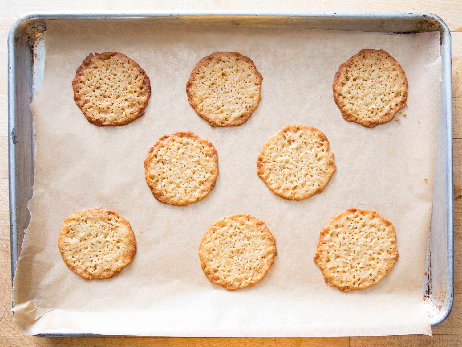 Overhead view of ricotta-brown butter cookies on a piece of parchment paper set in a baking sheet, after being removed from the oven.