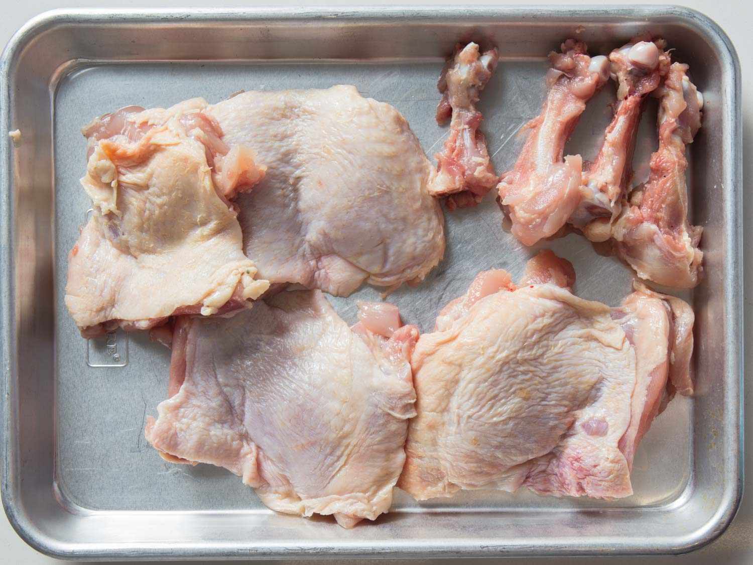 Deboned chicken thighs and bones on a baking sheet.
