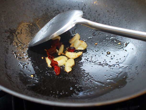 Chiles and garlic frying in a wok, stirred around by a metal spatula. 