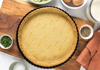 pate brisee on a wooden board, with bowls of eggs and butter to the side. 