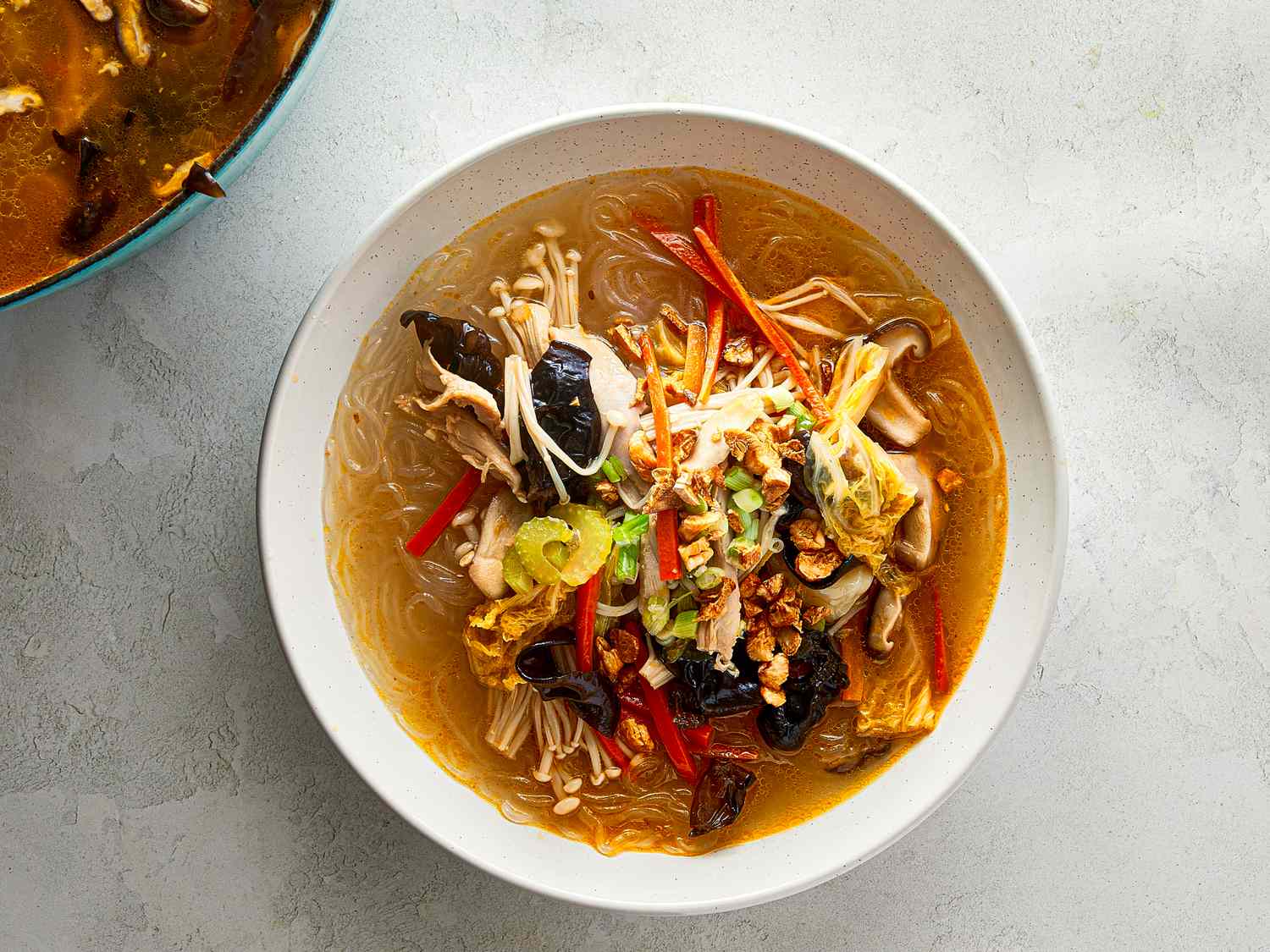 A bowl of chicken sotanghon soup garnished with vegetables and herbs presented on a light background