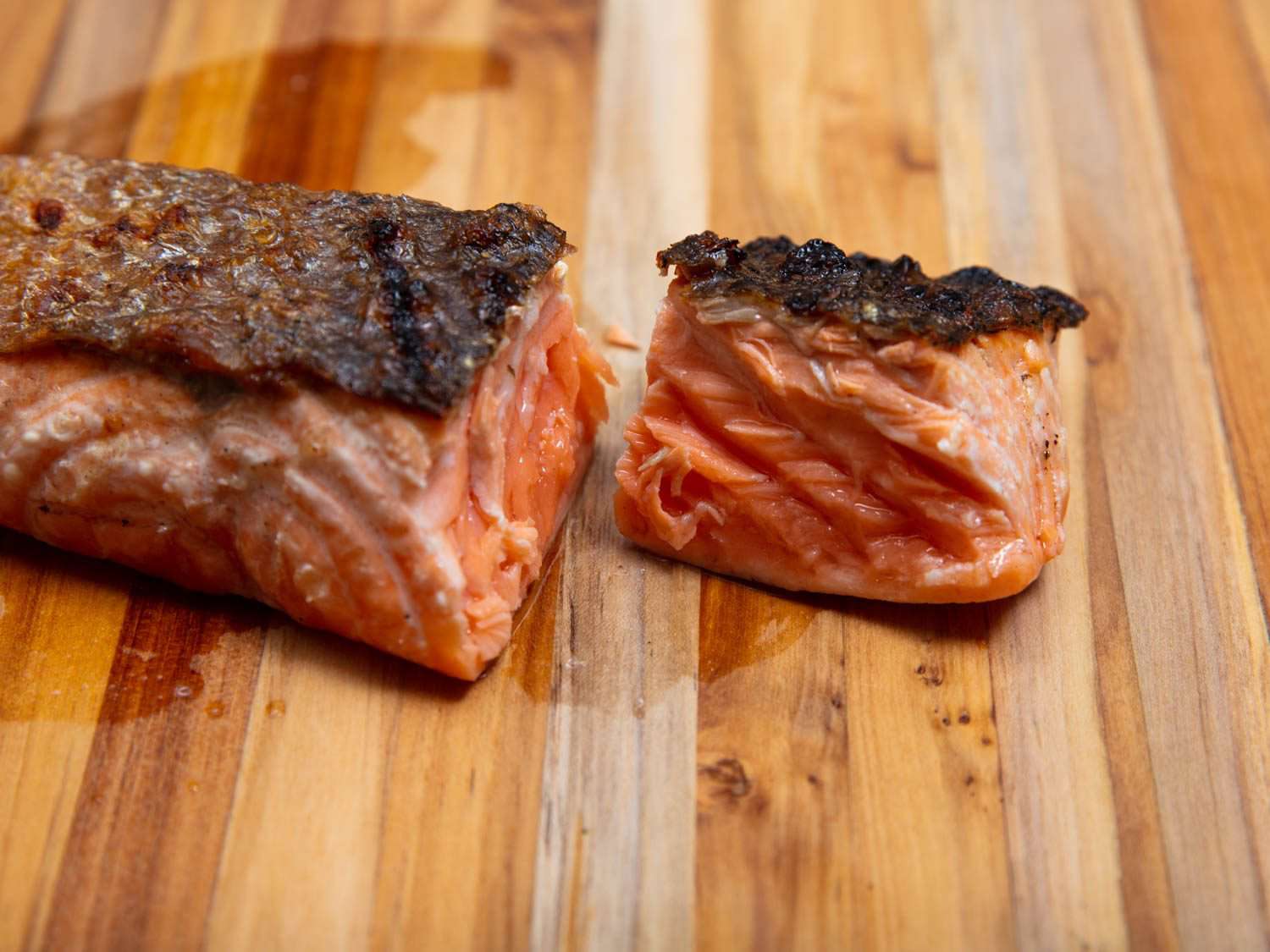 A piece of grilled salmon on a cutting board, showing a cross section to reveal a medium doneness, neither dry and well done nor rare.