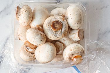 Container of fresh mushrooms on a marble surface