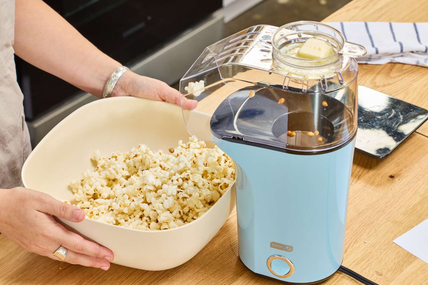 A person collects popcorn popped in the Dash Hot Air Popcorn Maker in a bowl