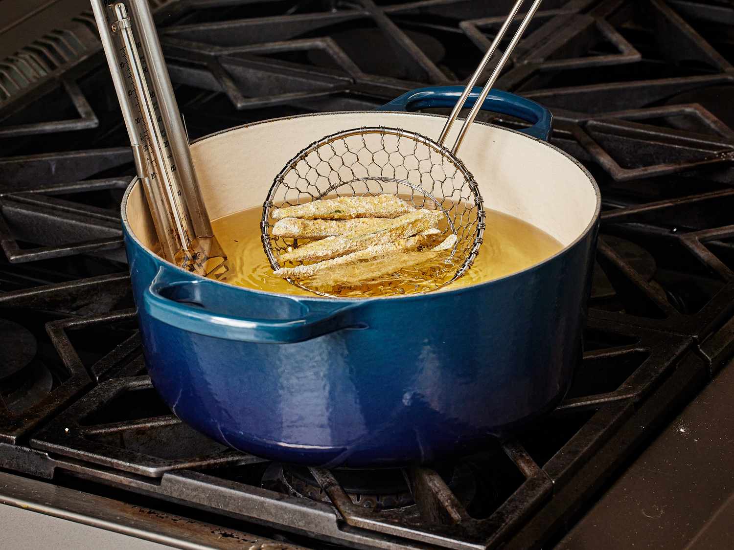 Fried okra being taken out of oil to drain with a spider strainer spoon 