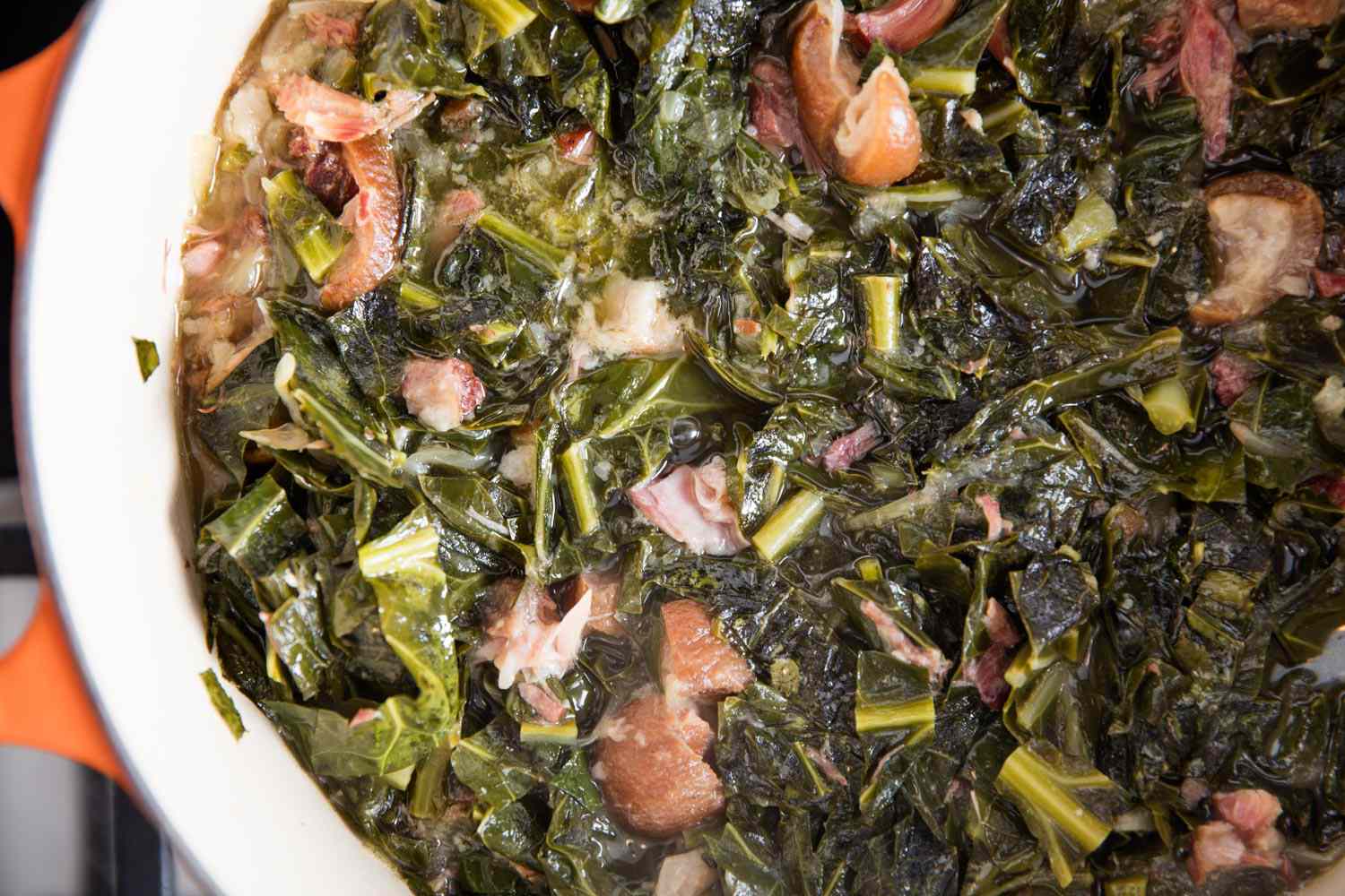 A Dutch oven of braised collard greens with ham hocks. 