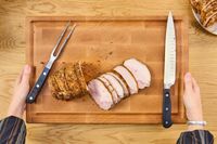 Hands holding a Boardsmith Maple End-Grain Cutting Board with sliced roast meat a carving fork and a knife