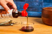 a person pouring kadoya sesame oil into a small glass cup