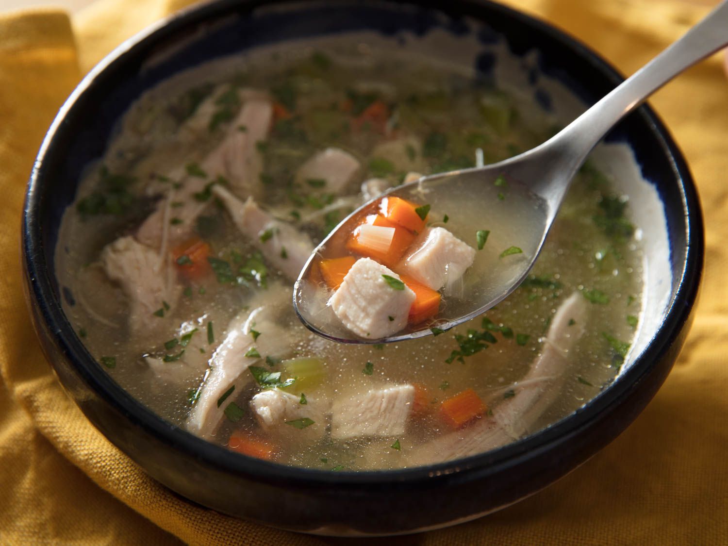 Close-up of a spoonful of chicken soup, with cubed chicken, carrots, and herbs.