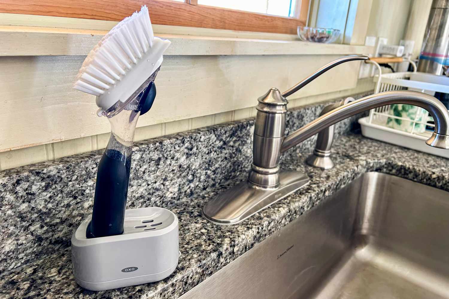 An OXO dishwashing wand in a plastic holder next to a kitchen sink