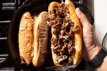 Philly cheesesteak in hand over skillet