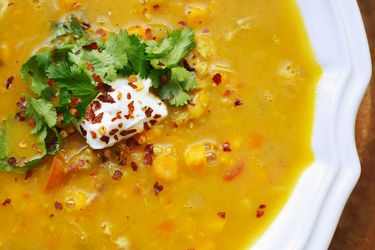 An overhead close-up of bright orange mulligatawny soup garnished with chile flake, fresh cilantro leaves, and a dab of yogurt.