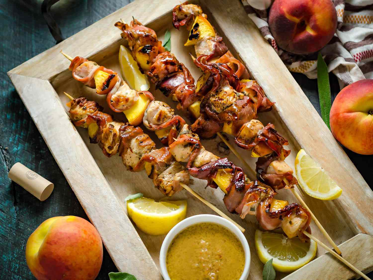 Skewered chicken and peaches on a wooden platter next to whole peaches.