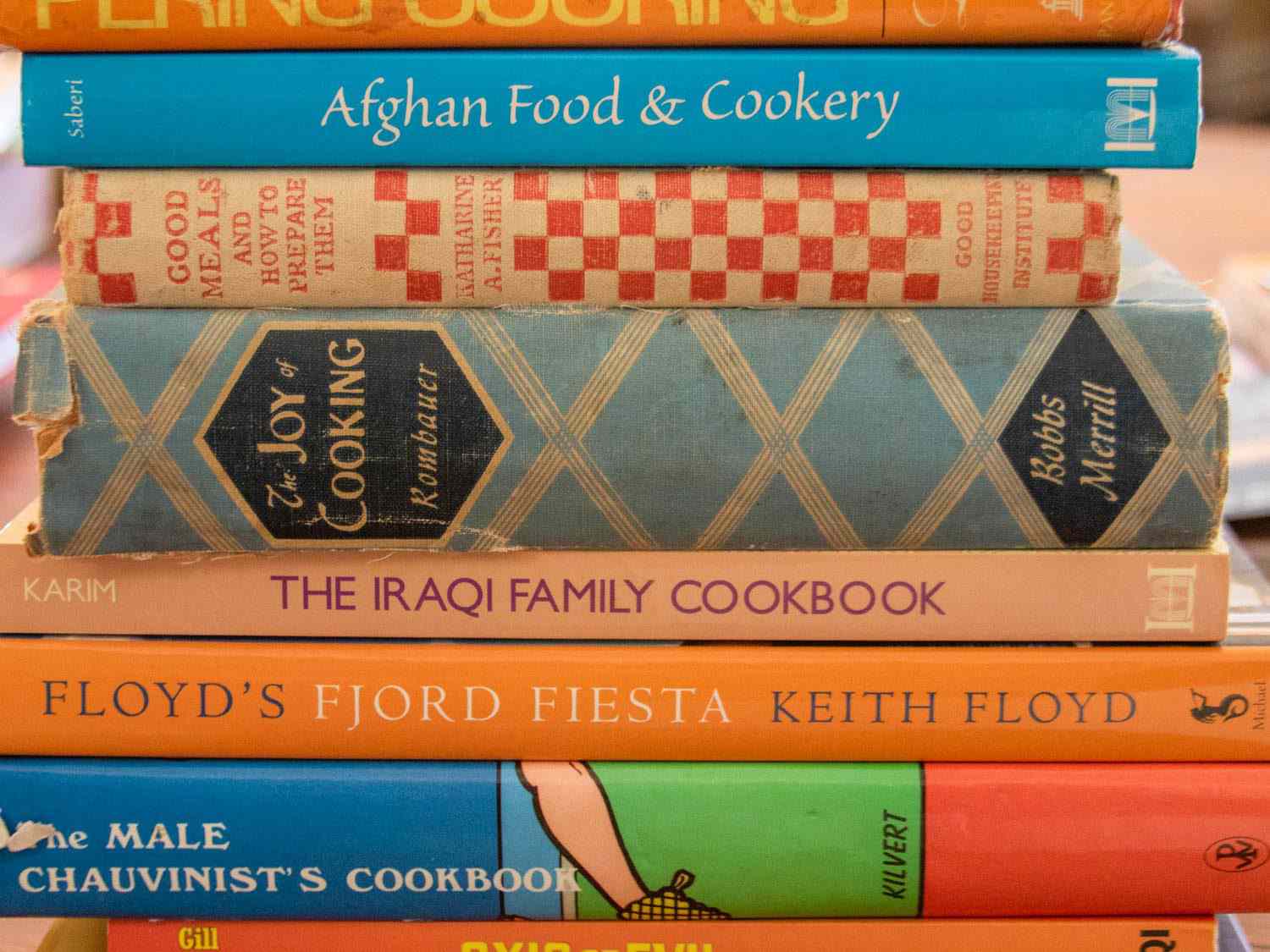 A stack of cookbooks from Sue Jimenez's collection, including Afghan Food & Cookery, The Iraqi Family Cookbook, and The Male Chauvinist's Cookbook.