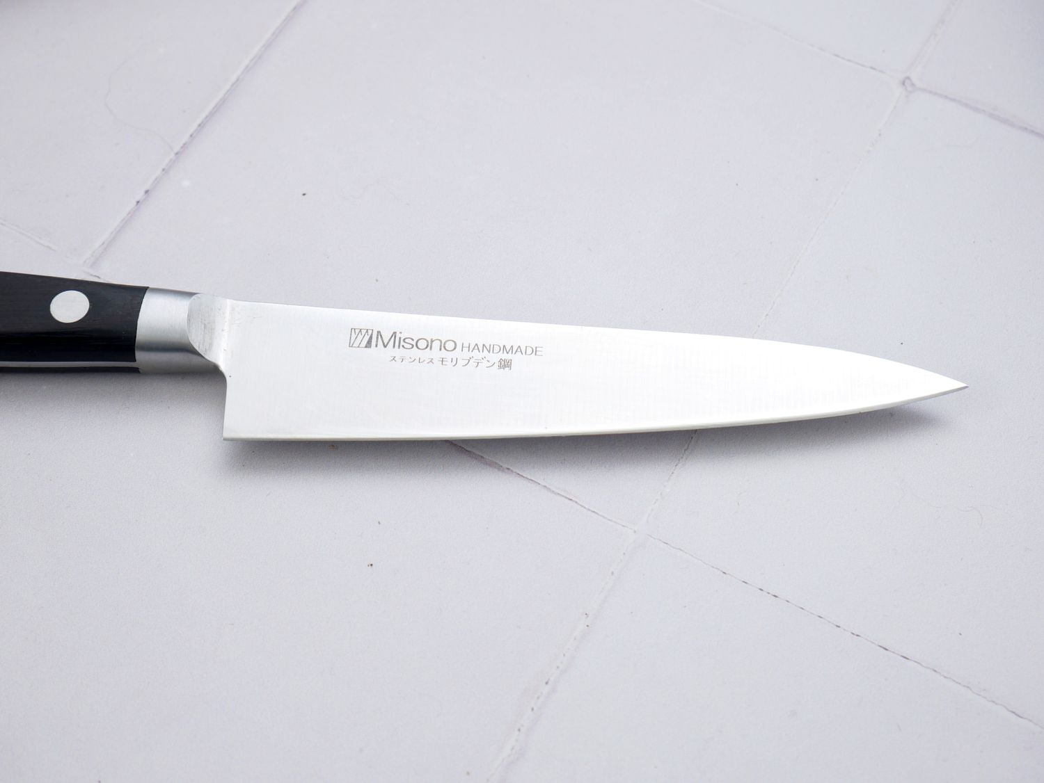 Misono petty knife with a black handle and stainless steel blade placed on a tiled surface