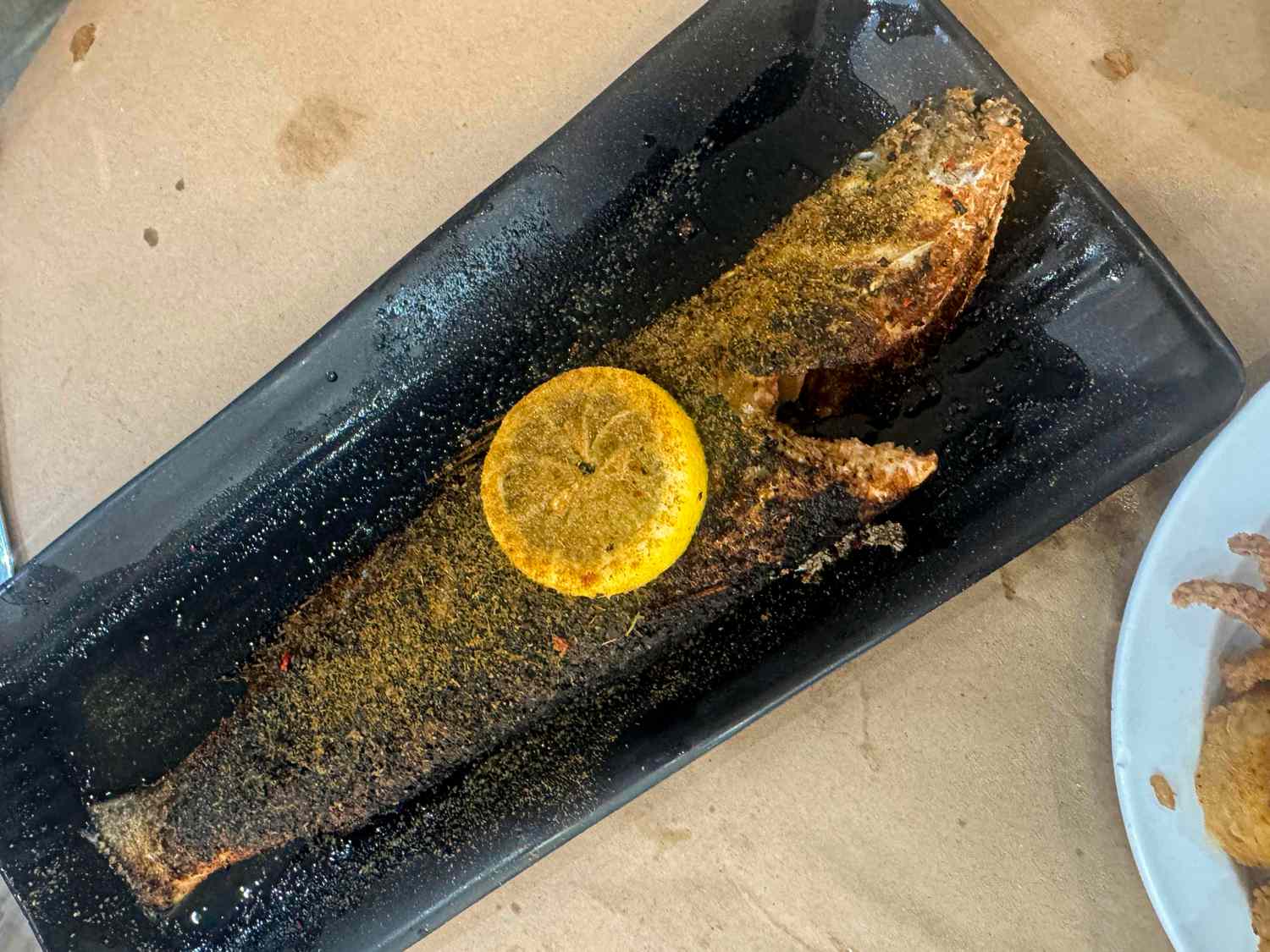 Cooked fish presented on a black rectangular plate garnished with a lemon slice