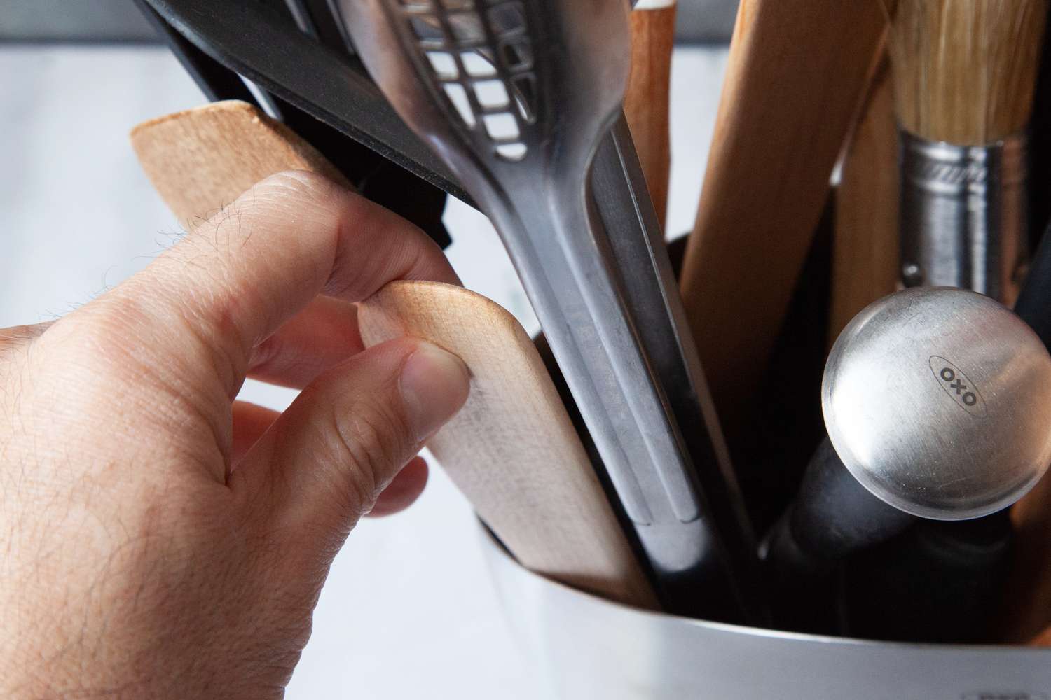 A hand pulling a wooden spoon out of a stainless steel utensil crock