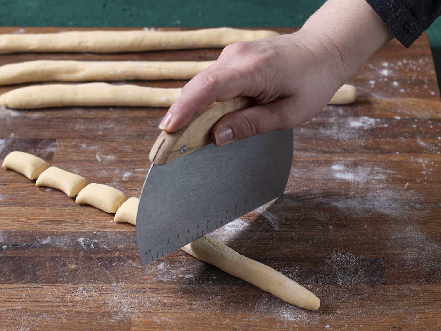 Logs of ricotta dough being cut into short gnocchi with a bench scraper.