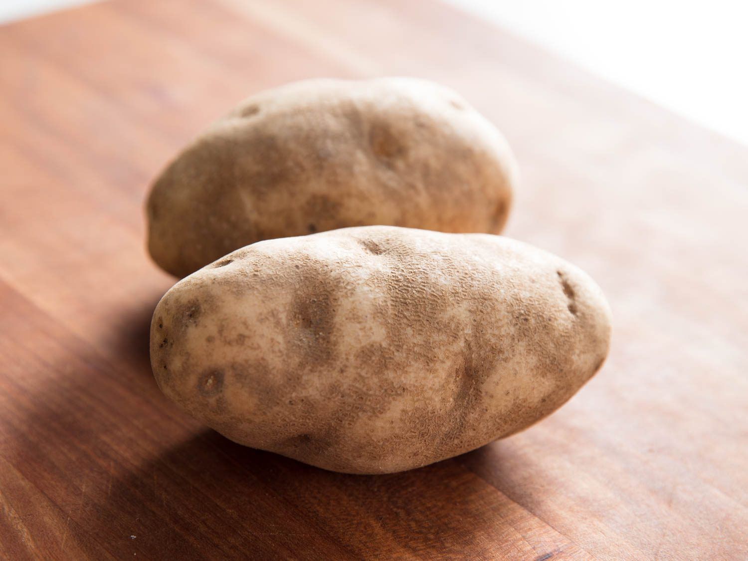Two russet potatoes on a wooden cutting board