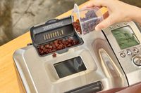 A person adding raisins to a compartment of the Breville Custom Loaf Bread Maker