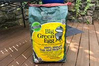 A bag of Big Green Egg natural oak and hickory lump charcoal on a wooden deck outdoors