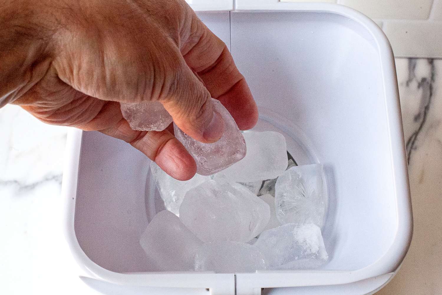 A hand adding ice cubes to a snow cone machine.