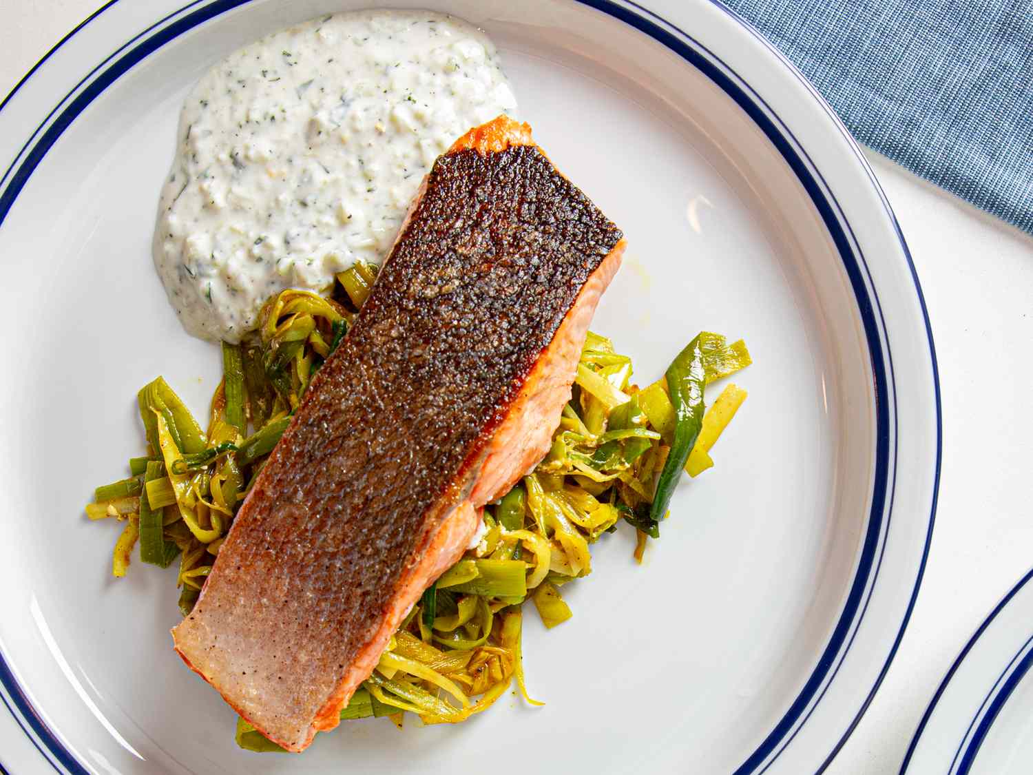 A plated dish of salmon with a crispy skin on a bed of leeks accompanied by a serving of sauce on the side