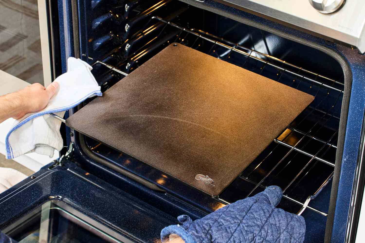 A person placing a pizza steel into the oven.