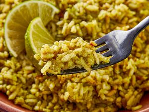 A fork holding a portion of seasoned rice with lime slices in the background