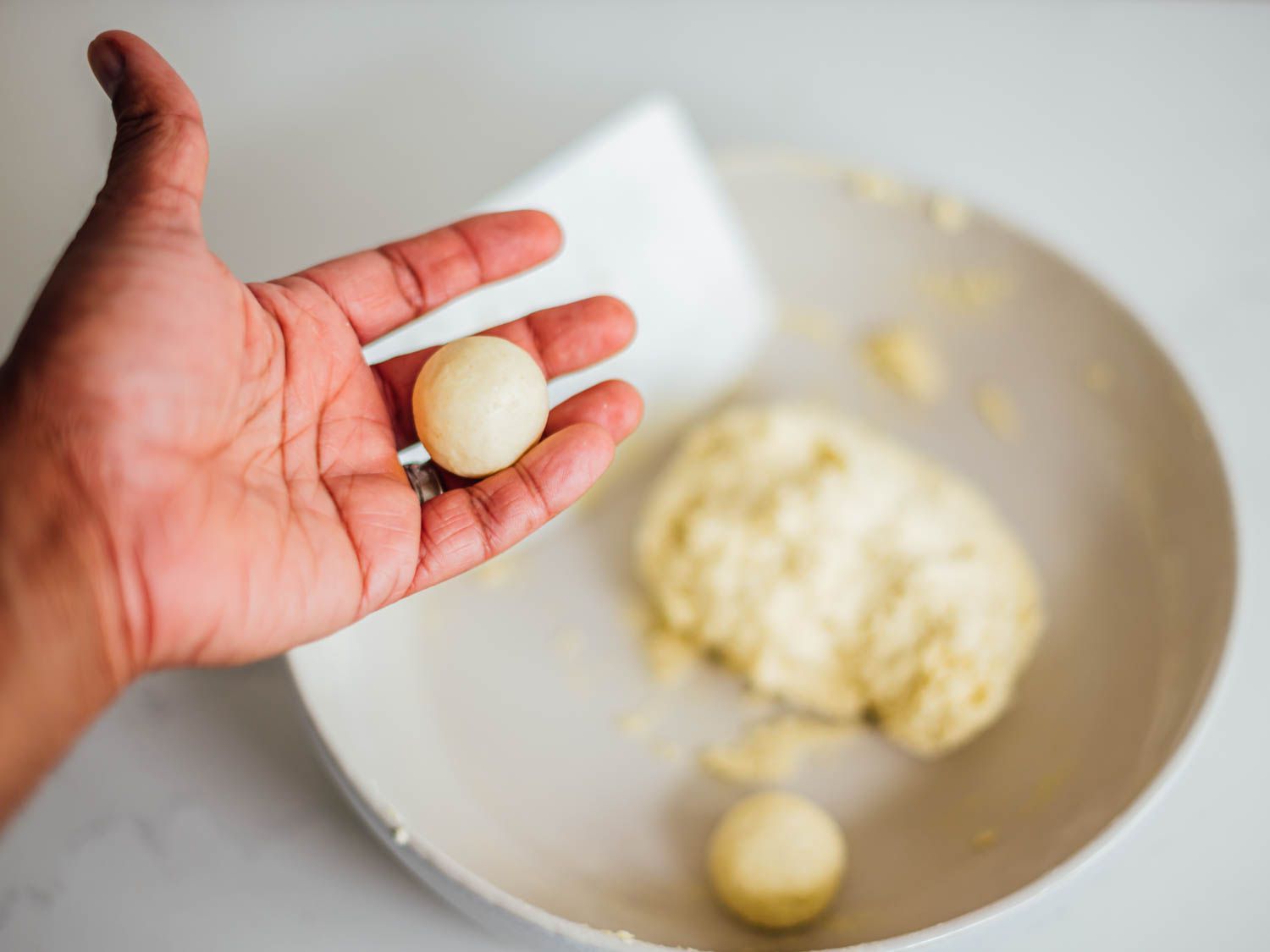 A hand holding a rolled bowl of gulab jamun dough, ready for deep frying.