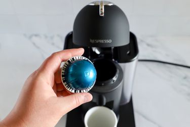 A hand holding an espresso pod in front of the Nespresso Vertuo Coffee and Espresso Machine by Breville
