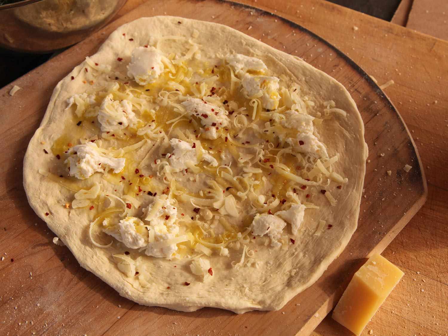 Torn mozzarella and shredded Gruyere cheese on a pizza dough slab.