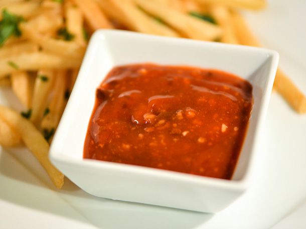 A square ramekin of orange chipotle ketchup flanked by a pile of french fries.