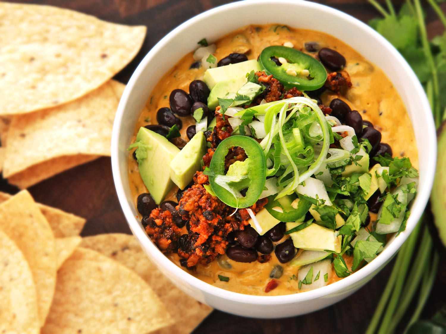 Overhead shot of a bowl of fully loaded vegan queso dip served with tortilla chips