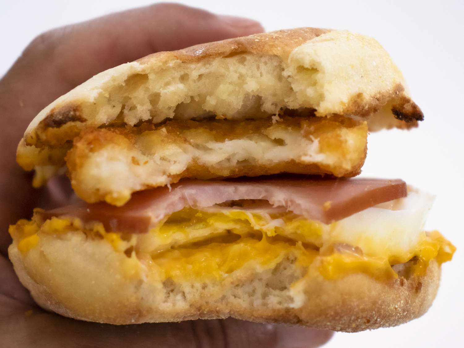 Hand gripping a McDonald's egg Mcmuffin with a hash brown inside, with a bite taken out of it