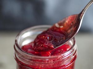A spoon dipping into a jar of strawberry jam.