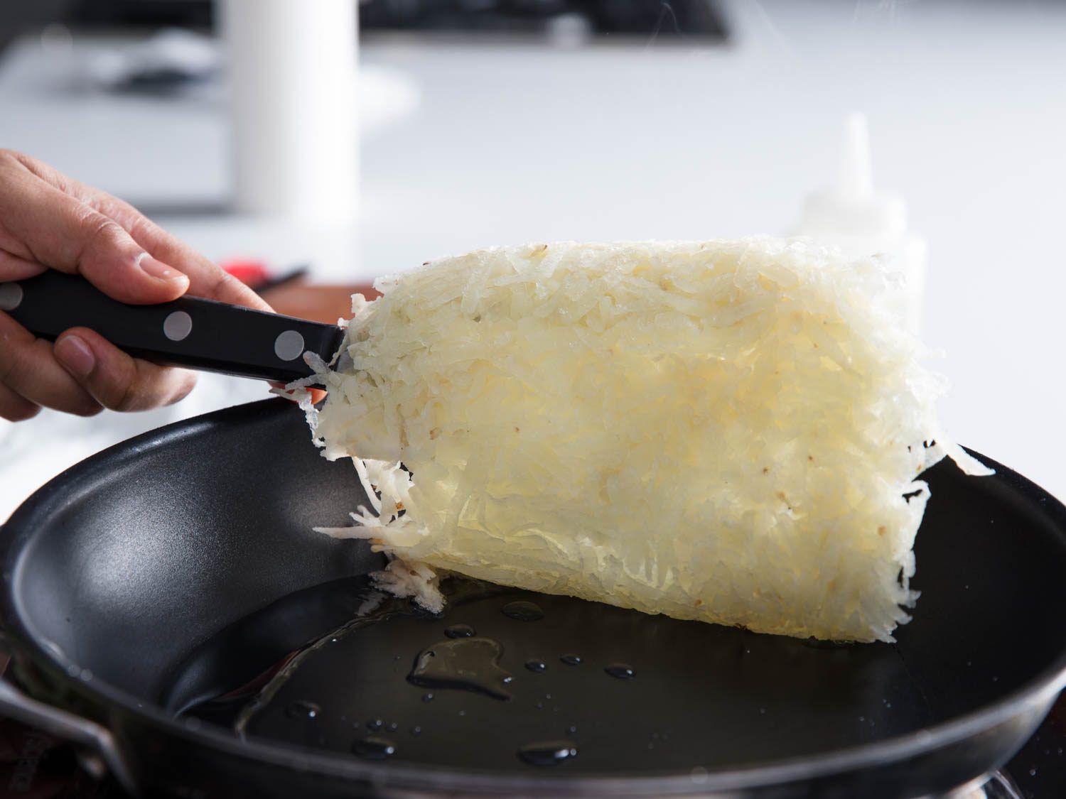 A pale mass of shredded hash browns being lifted up from a skillet by a spatula
