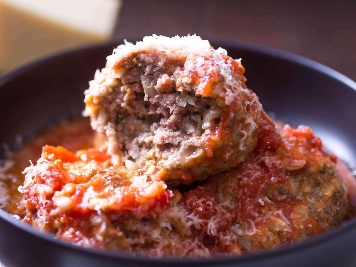 Closeup of ItalianAmerican meatballs topped with grated cheese served with a rich tomato sauce in a bowl