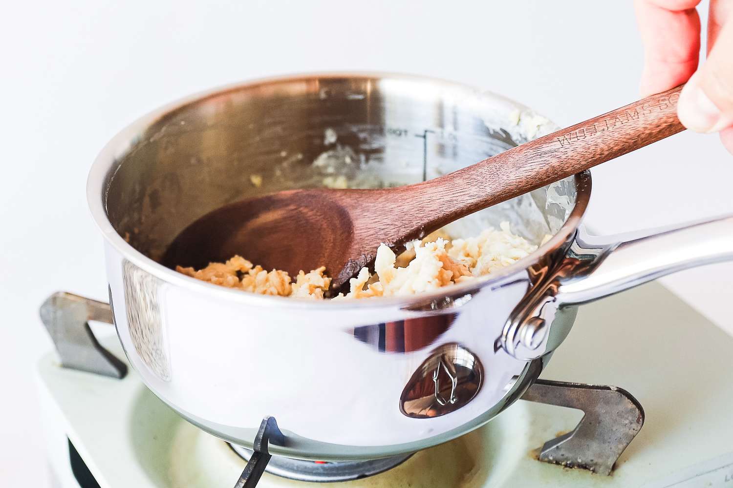 Hand holding a wooden spoon stirring oatmeal in a saucepan on a stove