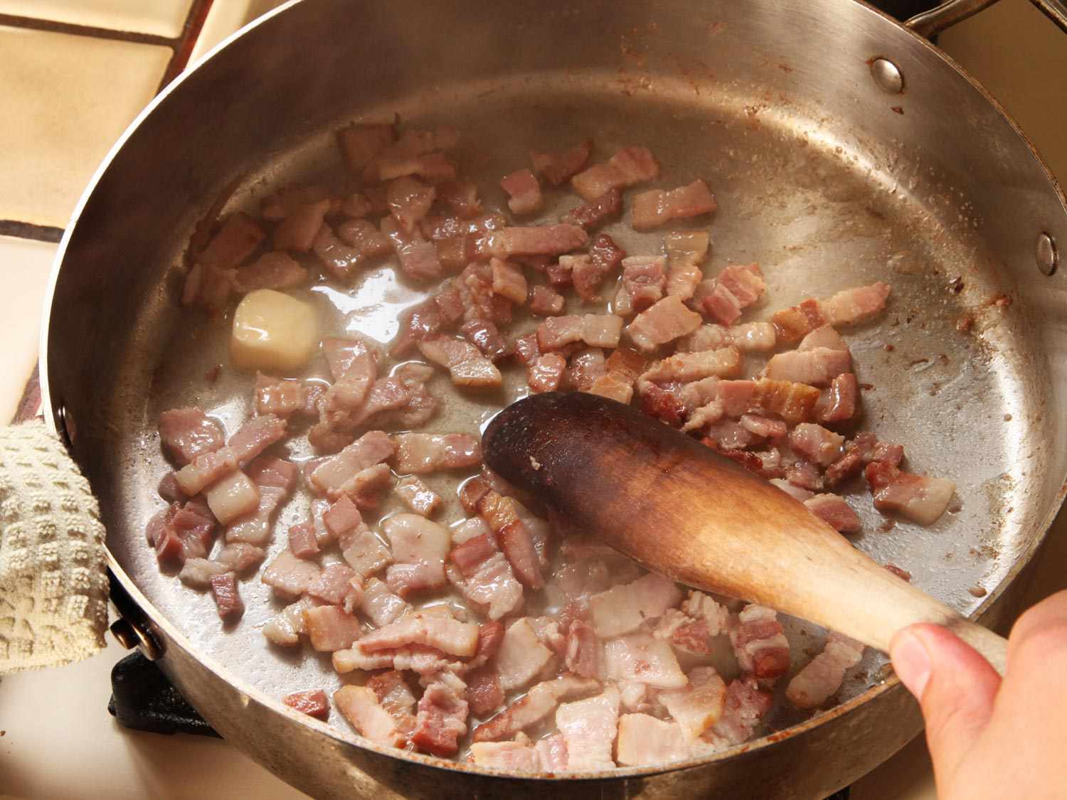Browning diced bacon in butter in a pan with wooden spoon